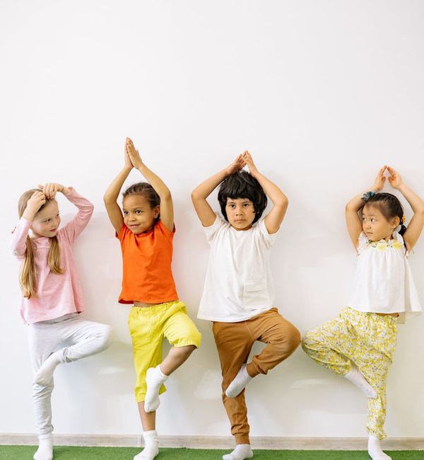 Child balancing on one leg in a tree yoga pose, smiling.